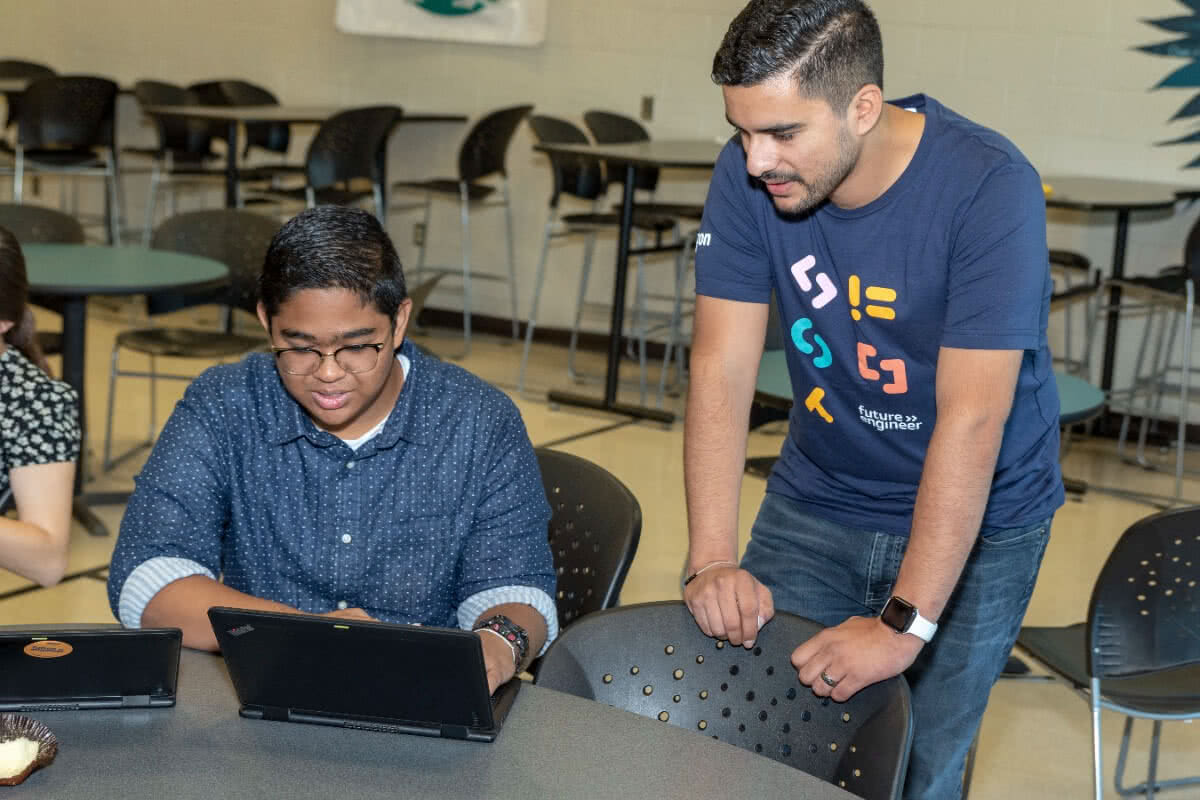 Teacher wearing an AFE t-shirt helping student at a computer
